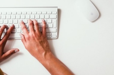 A person typing on a white keyboard at a clean desk, with a wireless mouse.