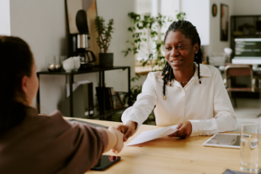 Two individuals shake hands across a desk, representing a moment of collaboration or agreement.