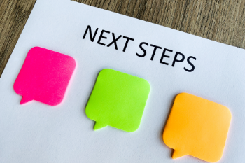 Paper with handwritten next steps and colorful sticky notes arranged around it, indicating a brainstorming session.