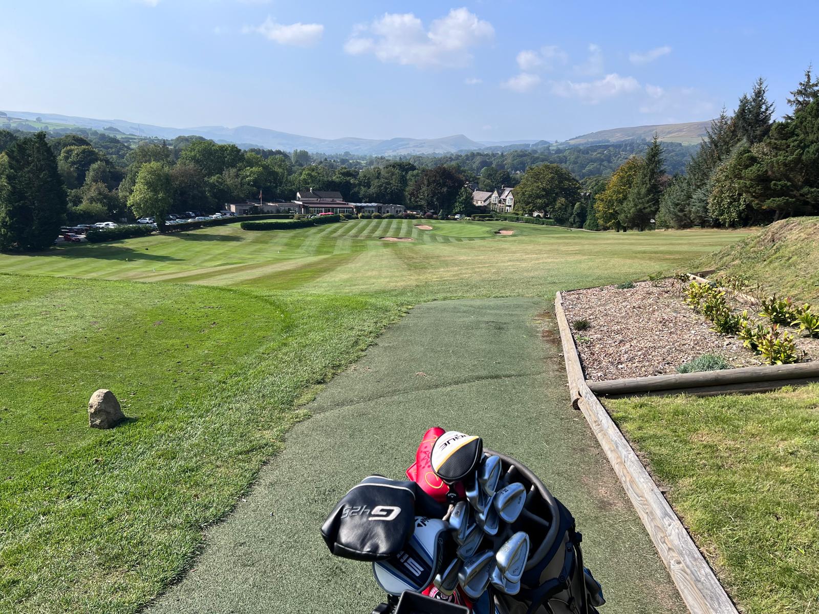 A golf bag on the grass, with a scenic green field of Sickleholme Golf Club in the Peak District in the background.