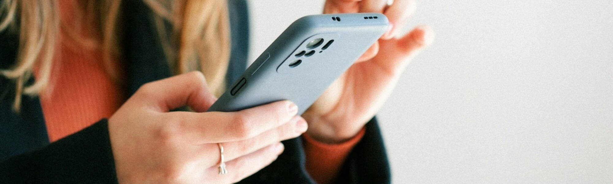 A woman holding a cell phone in her hand, looking engaged and focused on the screen.