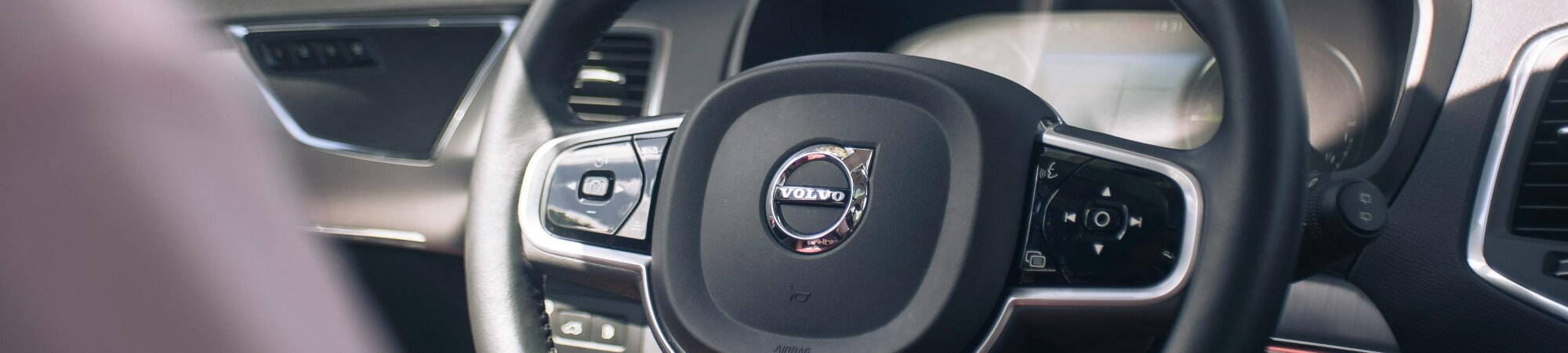 A man driving a Volvo car, focused on the road with the steering wheel prominently positioned in the center.