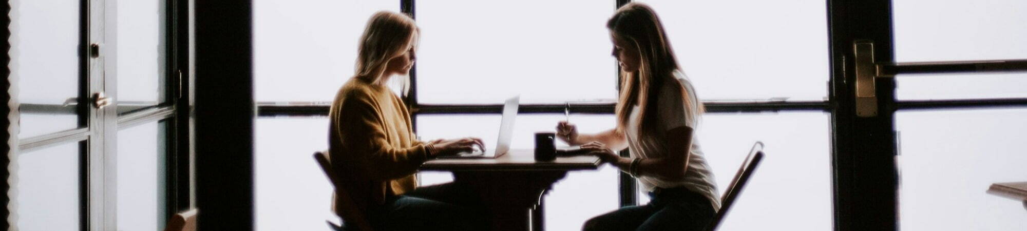 Two women sitting at a desk in an office, working together.