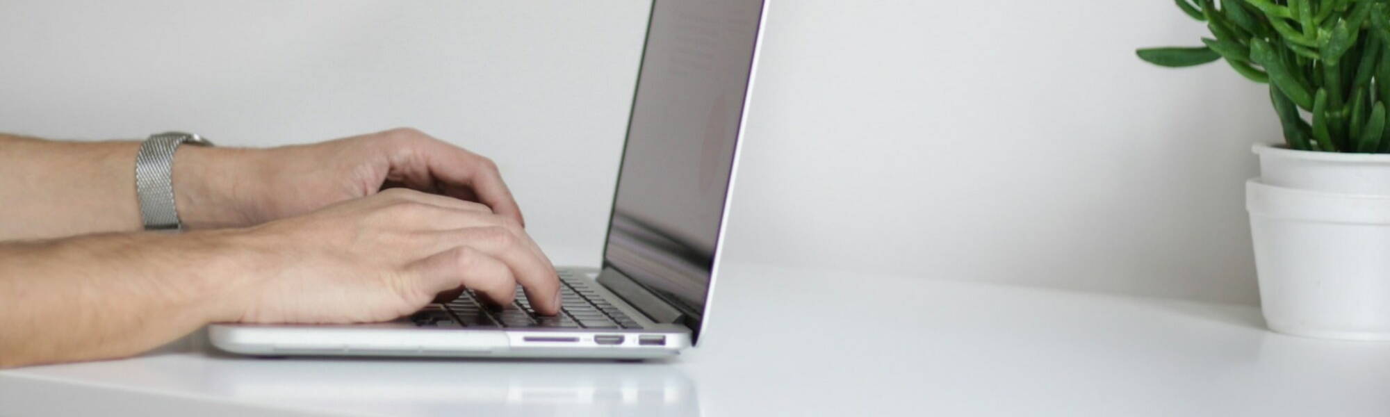 A person focused on typing on a laptop, with hands positioned over the keyboard, immersed in their work.