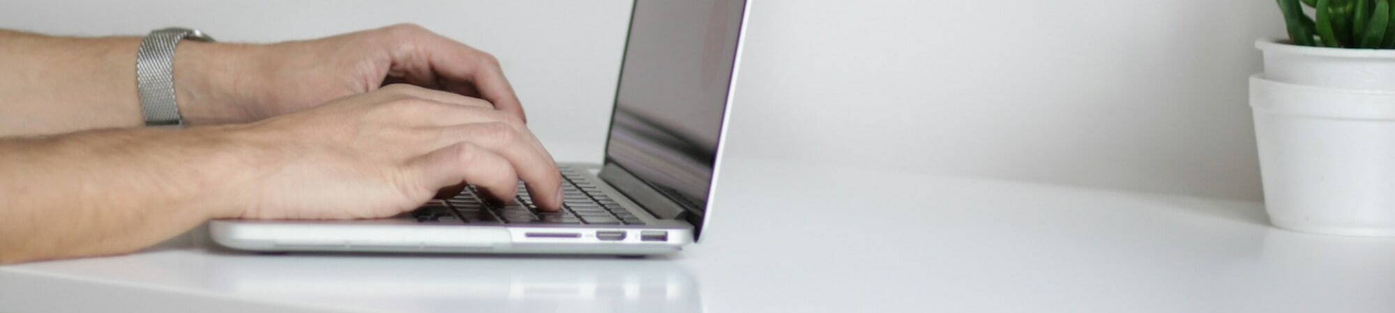 A person focused on typing on a laptop, with hands positioned over the keyboard, immersed in their work.